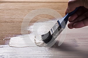 Hand holding a brush applying varnish paint