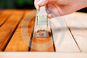 hand holding a brush applying varnish paint on a wooden garden table - painting and caring for wood