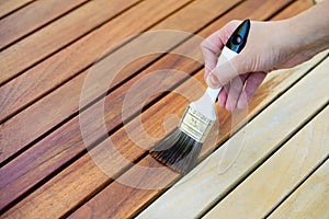 hand holding a brush applying varnish paint on a wooden garden table - painting and caring for wood