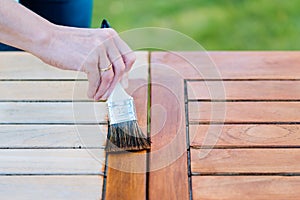 Hand holding a brush applying varnish paint on a wooden garden table - painting and caring for wood photo