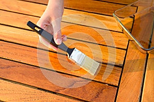Hand holding a brush applying varnish paint on a wooden garden table photo