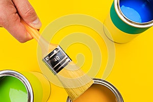 Hand holding Brush  on open can of paint on yellow background. Renovation concept - Image