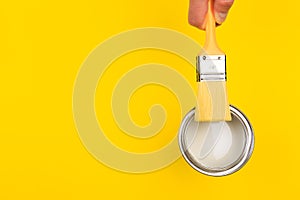 Hand holding Brush  on open can of paint on yellow background. Renovation concept - Image