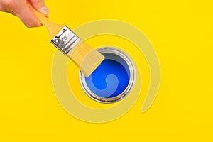 Hand holding Brush  on open can of paint on yellow background. Renovation concept - Image