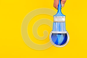 Hand holding Brush  on open can of paint on yellow background. Renovation concept - Image