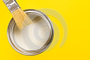 Hand holding Brush  on open can of paint on yellow background. Renovation concept - Image