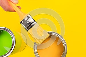 Hand holding Brush  on open can of paint on yellow background. Renovation concept - Image