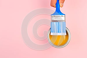 Hand holding Brush  on open can of yellow  paint on pastel pink background. Renovation concept - Image