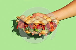 Hand holding bubble waffle vegetarian with tomato, lettuce,  sauce, cream cheese, red bell pepper  on green background.