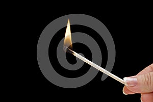Hand holding burning match stick on black