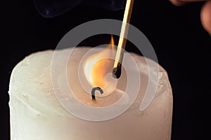 Hand holding burning match stick lighting candle on black background. Match with the flame and candle in dark room close up