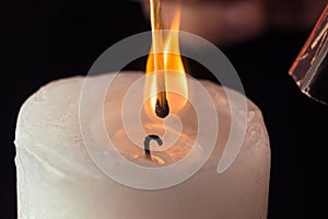 Hand holding burning match stick lighting candle on black background. Match with the flame and candle in dark room close up