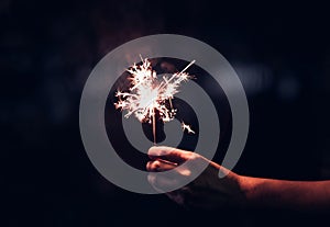 Hand holding burning Sparkler blast on a black background at night,holiday celebration event party,dark vintage tone. photo