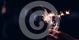 Hand holding burning Sparkler blast on a black bokeh background