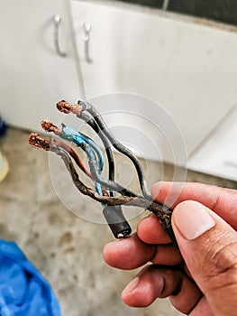 Hand holding burnt and melt down wires from heavy usage electrical device.