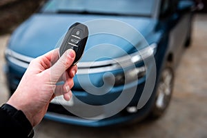 Hand holding a car key with remote control and pushing a button, he is unlocking the door