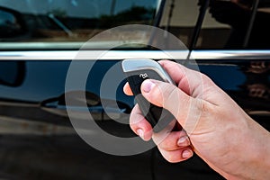 Hand holding a car key with remote control and pushing a button, he is unlocking the door.