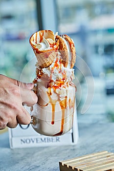 Hand holding a caramel ring milkshake with cookies and ice cream cone