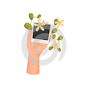 Hand is holding a card with a poloroid and a stem with leaves and flowers. Vector illustration on white background.