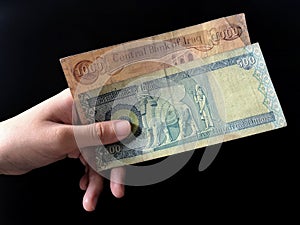 Hand holding a Central Bank of Iraq 1000 and 500 Dinars over black background