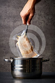 Hand holding chicken breast over cooking pot photo