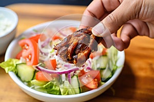 hand holding a chili marinated wing over a bite-sized salad