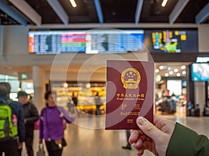 Hand holding a Chinese passport with airport departure hall as background
