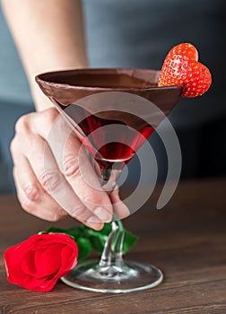 A hand holding a chocolate rimmed Valentine& x27;s Day cocktail in a martini glass.