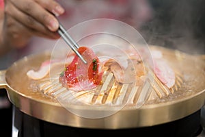 Hand holding chopstick with grilled korean pork grilled yakiniku japanese style.