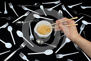 Hand holding chopsticks in bowl with noodles on black background