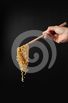 Hand holding chopsticks and noodles on black background