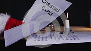 Hand holding Christmas carols music song sheet by candlelight