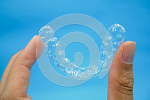 Hand holding clear plastic retainer teeth that isolated on blue sky background. it`s an equipment for orthodontist give the