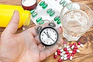 Hand holding clock over table with pills and glass of water