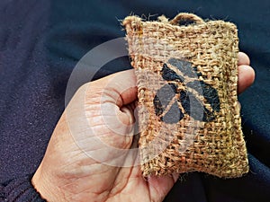 A hand holding a coffee car perfume filled with coffee beans, packaged in an aesthetically pleasing rough burlap material