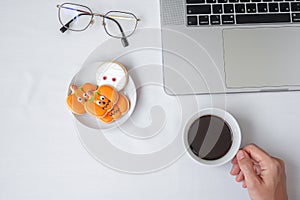 Hand holding coffee cup and eating Halloween Cookies during using computer laptop. Happy Halloween, online shopping, Hello October