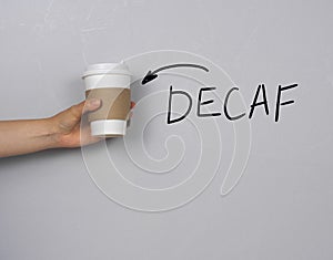 hand holding coffee to go cup against concrete gray wall with text decaf