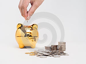 Hand holding coin into golden piggy bank with stack of coin