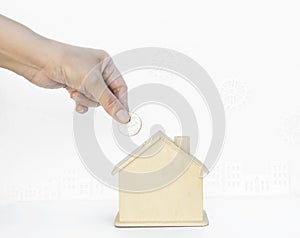 Hand holding coin with house piggy bank on white background with gear and builiding pattern background