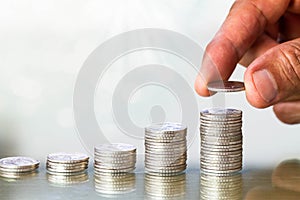 Hand holding coin putting on top of coin`s stack