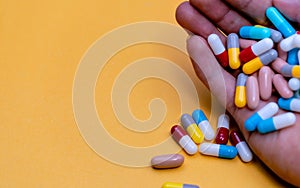 Hand holding colorful capsule pills on yellow background. Antibiotic drug overuse concept. Antibiotic drug resistance and superbug