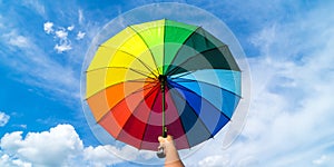 Hand holding colorful rainbow umbrella and blue sky background. LGBT, Pride Month, diversity, Sunprotect Concept