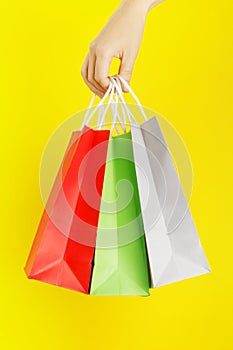 Hand holding colourful shopping or gift bag against yellow background