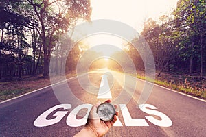 Hand holding compass on Empty asphalt road and Goals concept