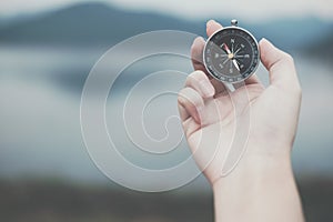 hand holding compass for searching direction outdoor. man seeking way with nature background. travel lifestyle, summer vacation c