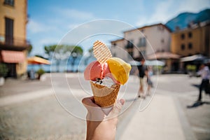 Hand holding cone with colorful delicious italian gelato ice-cream in Menaggio town near Como lake