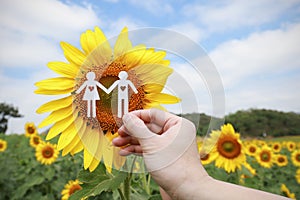 Hand holding couple made from paper over sunflower filed