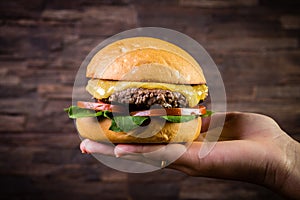 Hand holding a craft beef burger with cheese, rocket leafs and french fries on rustic background