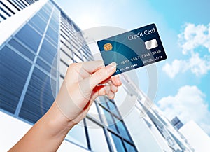 Hand holding credit card against builind and sky