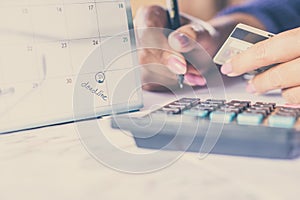 Hand holding credit card calculating her monthly expenses with deadline calendar